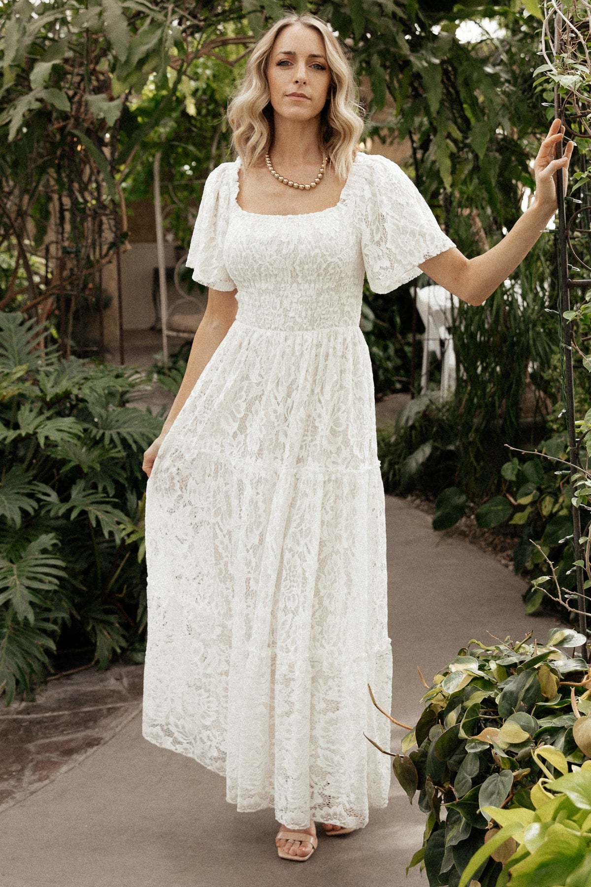 Model wearing off-white lace maxi dress showing tiered skirt movement and short bell sleeves on a neutral background.