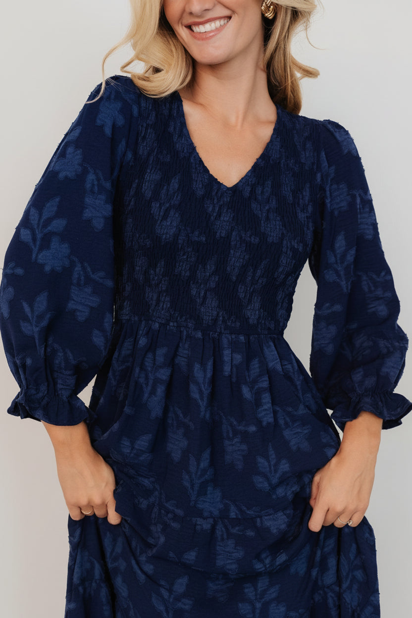 Close-up detail of textured burnout fabric and navy floral print with visible smocking, ruffle cuff, and V-neck stitching.