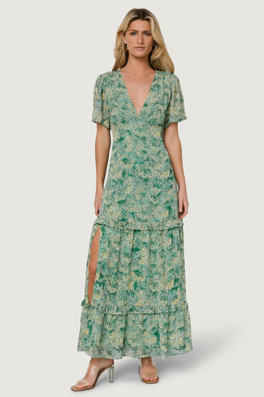 Front view of model wearing green floral chiffon deep V maxi dress with tiered ruffle skirt and right-side slit, shown full length.