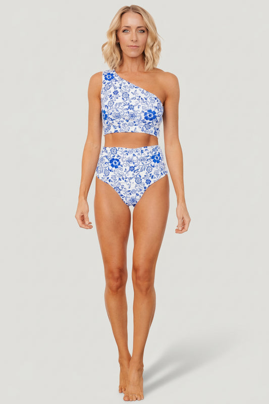Front view of white and cobalt floral high-rise bikini bottom with ruched sides and cheeky high-cut silhouette on a neutral backdrop.
