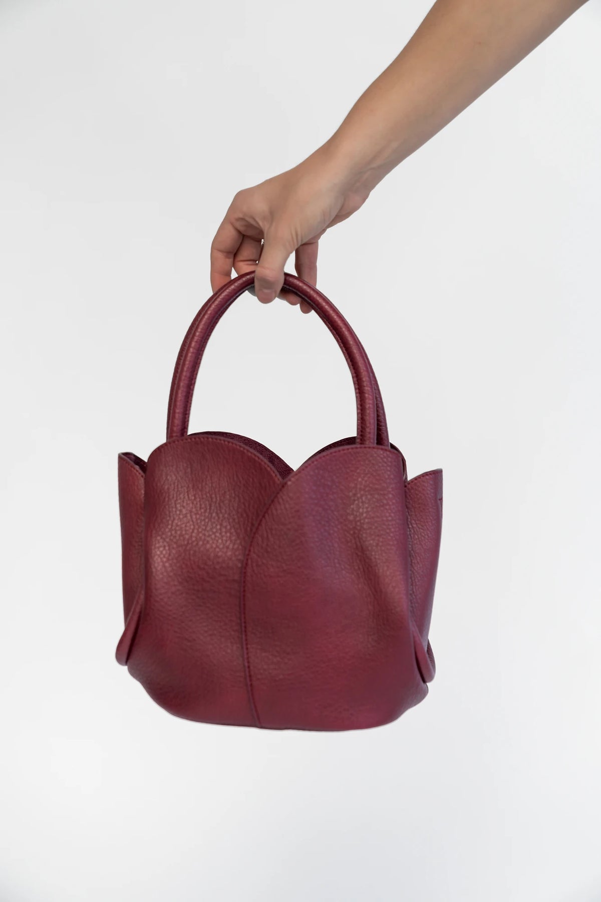 Beloved Tulip Tote Bag in Wine with a soft pebbled texture, tulip-inspired panel detailing, and rounded top handles.