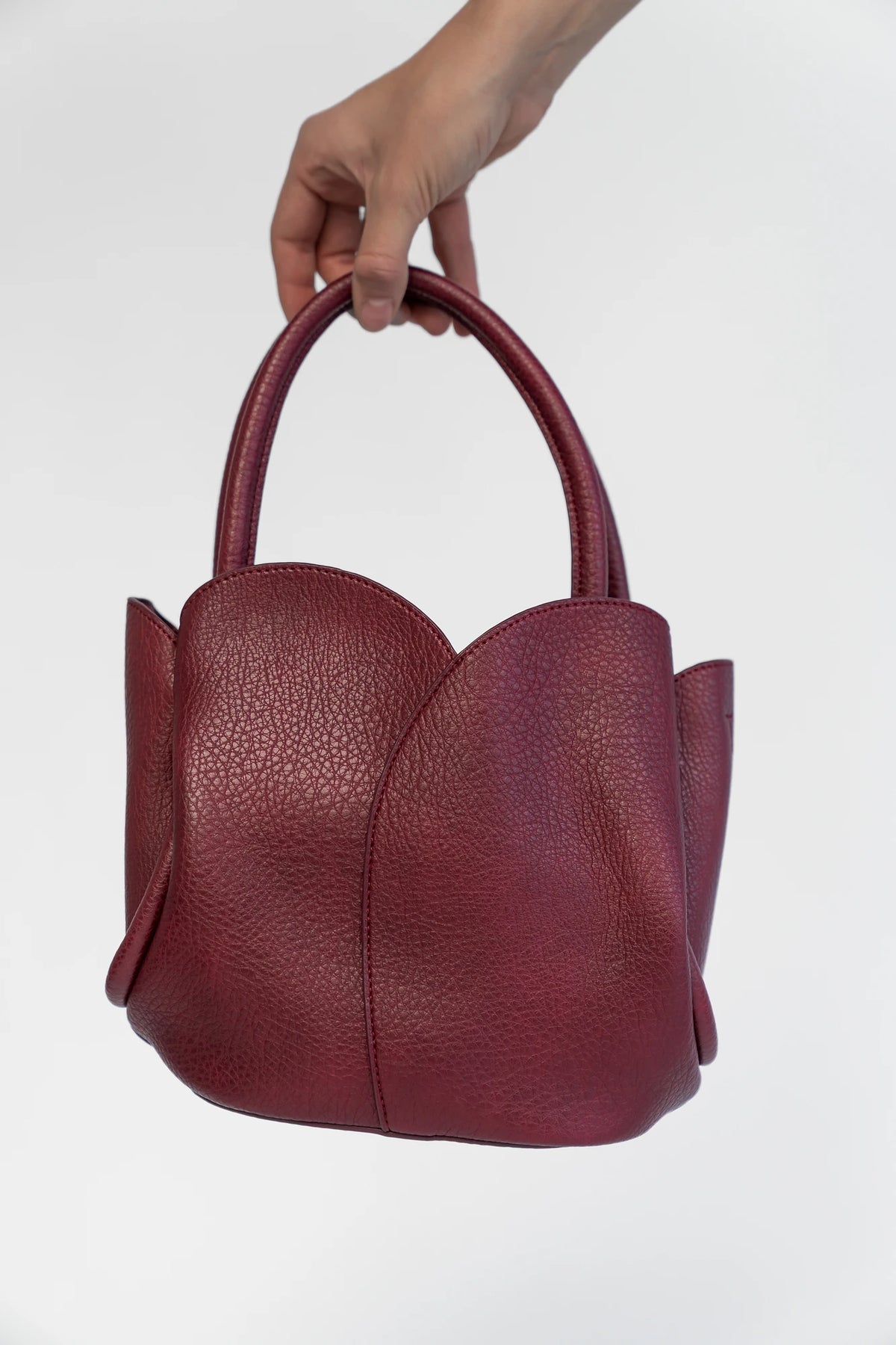 Beloved Tulip Tote Bag in Wine with a soft pebbled texture, tulip-inspired panel detailing, and rounded top handles.