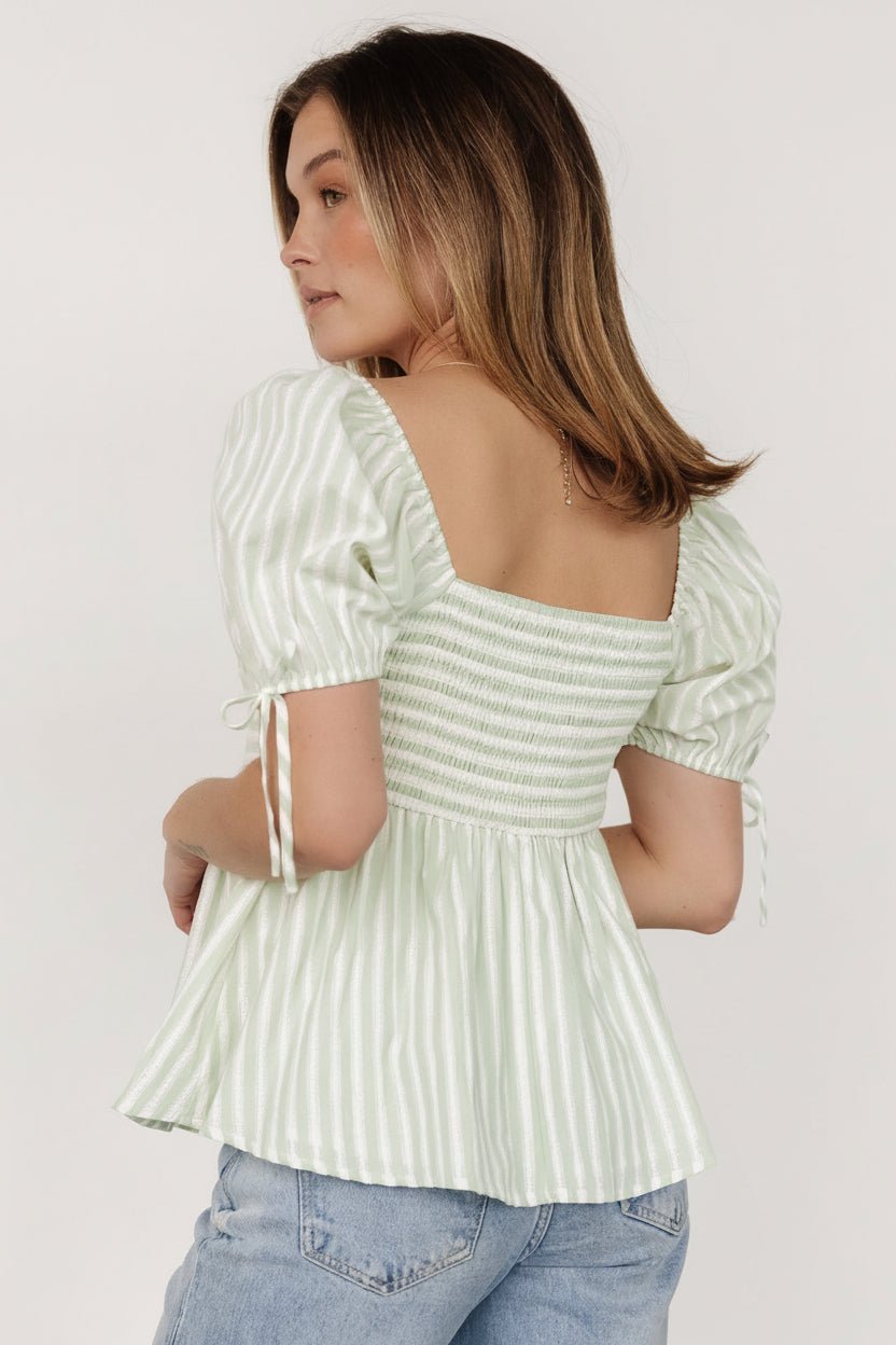 Styled flat-lay of Betsy Peplum Top in green and white stripes with peplum hem and embroidered stripe accents.