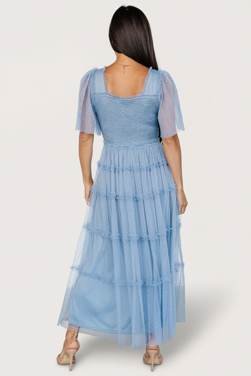 Back view showing elastic square back and smocked bodice stretch, with tiered ruffle midi skirt movement in dusty blue dotted tulle.