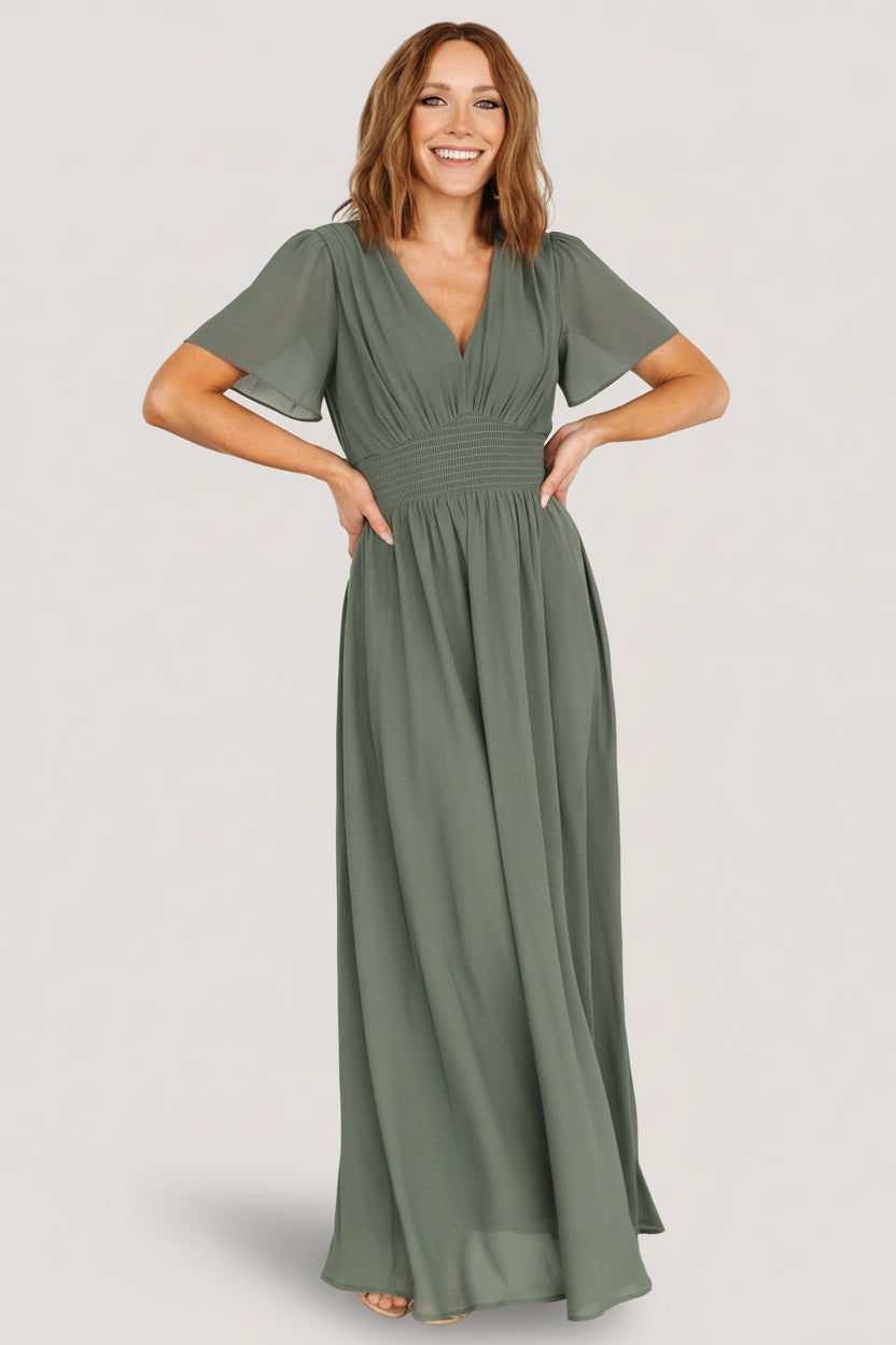 Model front view wearing Birdie Maxi Dress in dark sage with V-neck, smocked waist, short flutter sleeves and flowing chiffon hem.