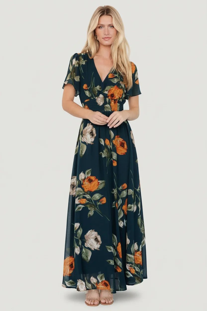 Model wearing deep topaz floral Birdie Maxi Dress with V-neck, smocked waist and flutter sleeves, full-length view, front pose.