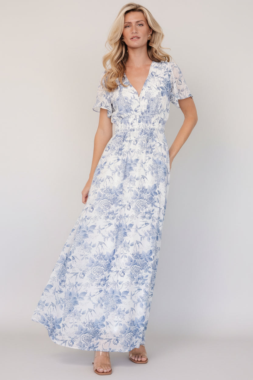 Front view of off-white chiffon maxi dress with light blue floral print, V-neckline, short flutter sleeves, and smocked waist.