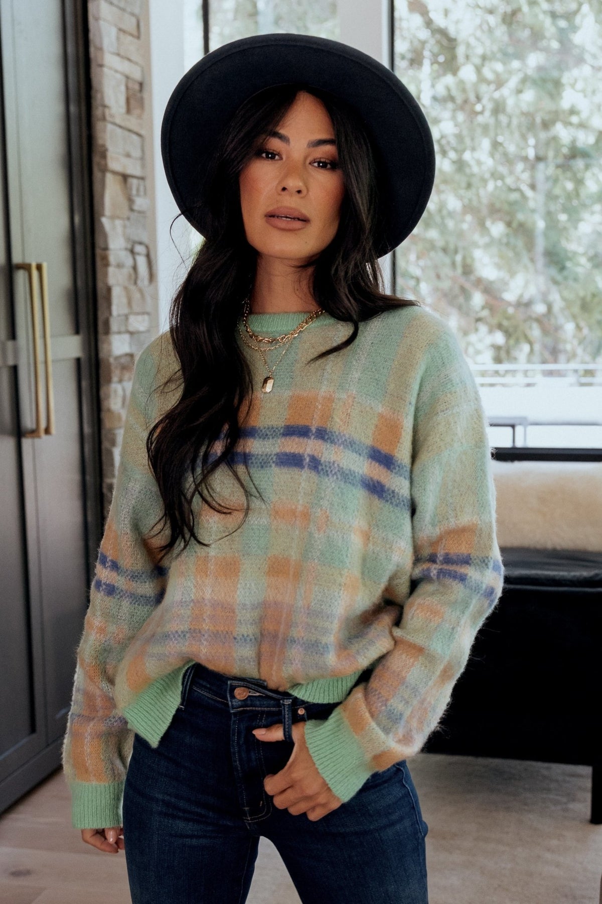 Close-up detail of the chunky knit texture and plaid yarns in green, camel, blue, and purple with visible ribbed cuff and hem.
