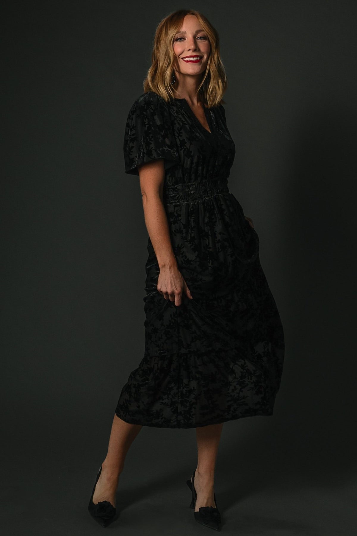 Side view of the Bronwyn midi dress in black highlighting a hidden side pocket and the two-tier skirt drape.