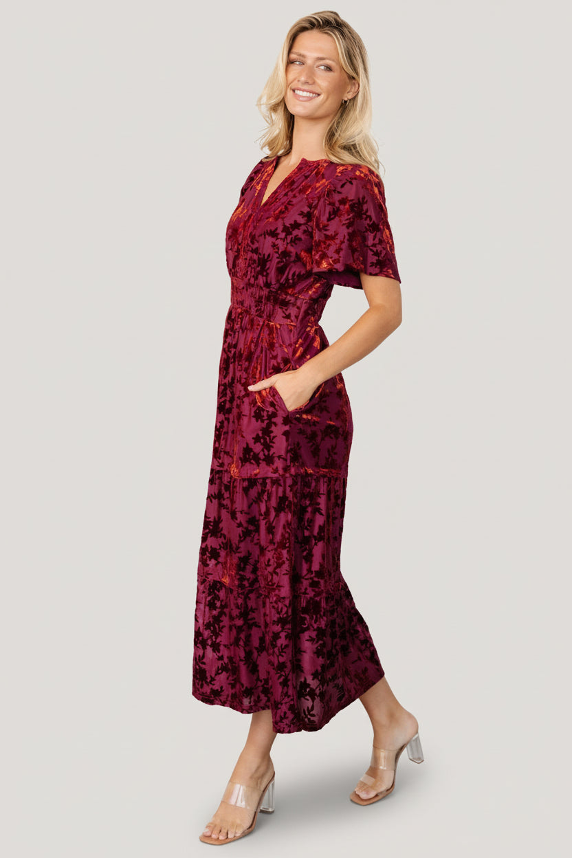 Model styling Bronwyn rust floral dress with hands in hidden side pockets, demonstrating pocket placement and relaxed midi length.