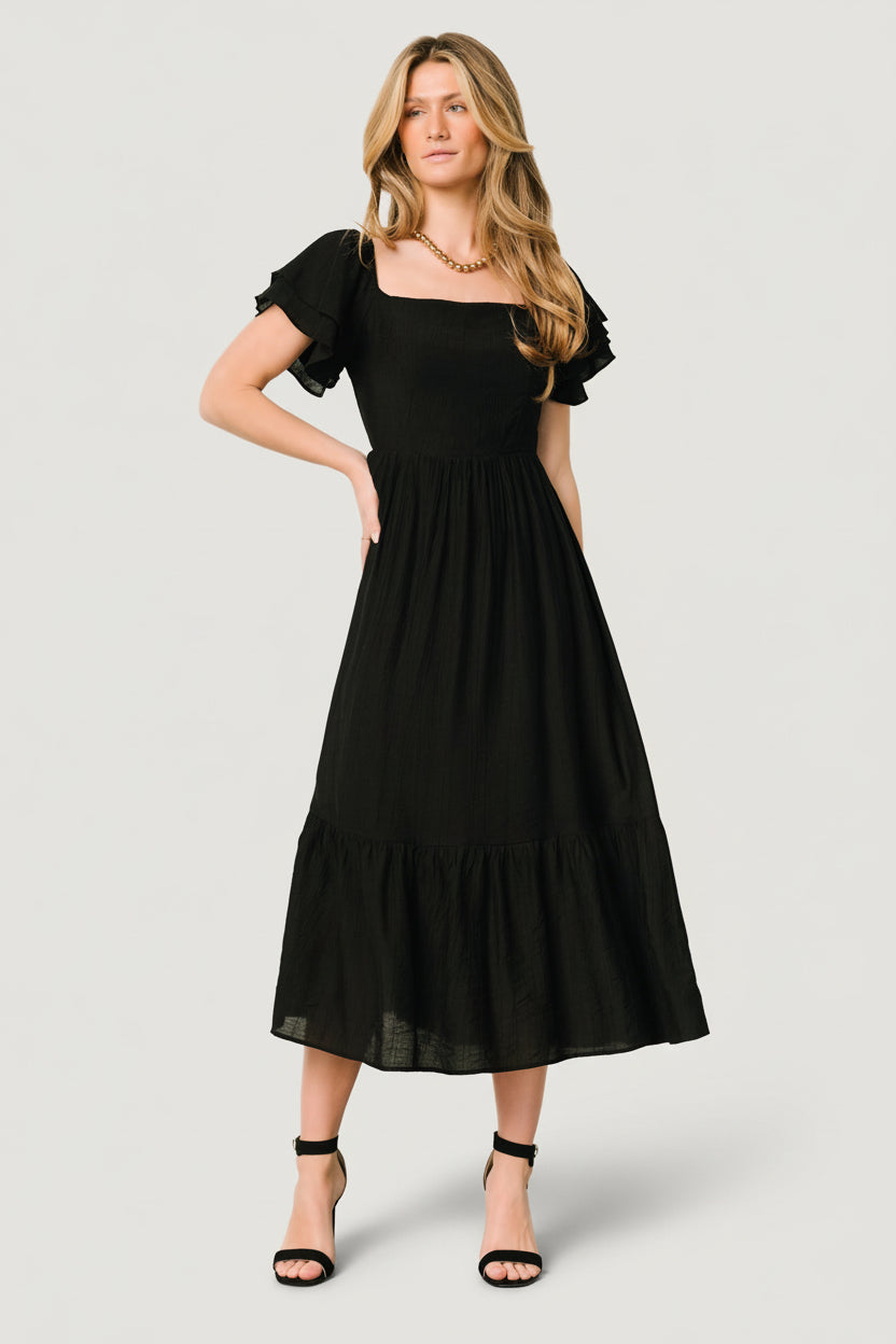 Side view of the black midi dress highlighting the ruffle-tier skirt, lining coverage, and gentle A-line shape.