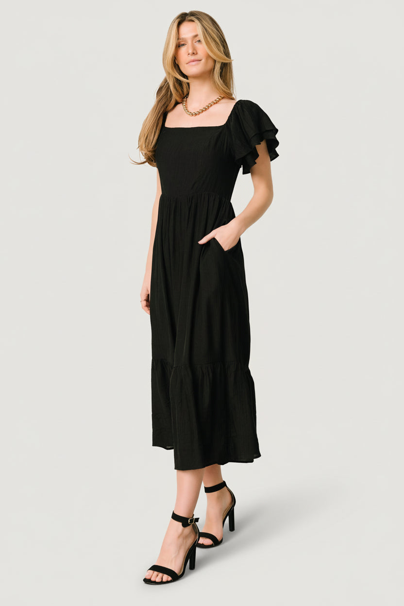 Close-up of the square neckline and tiered ruffle sleeve detail on the black textured woven fabric.