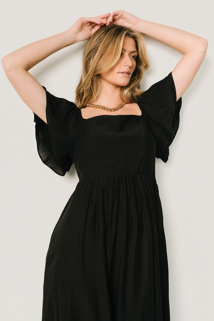 Three-quarter model view showing the smocked back bodice, elastic shoulders, and midi skirt with ruffle tier and soft drape.