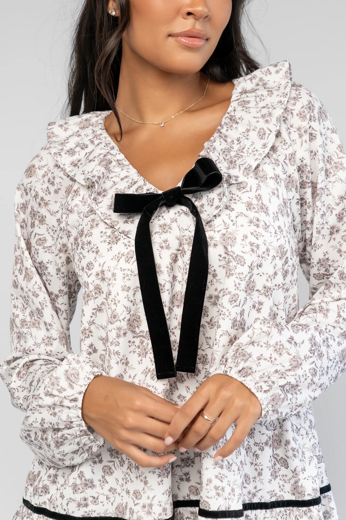 Caprice Bow Front Short Dress in Ivory Floral with V-neckline, ruffled trim, black velvet bow, and long sleeves.