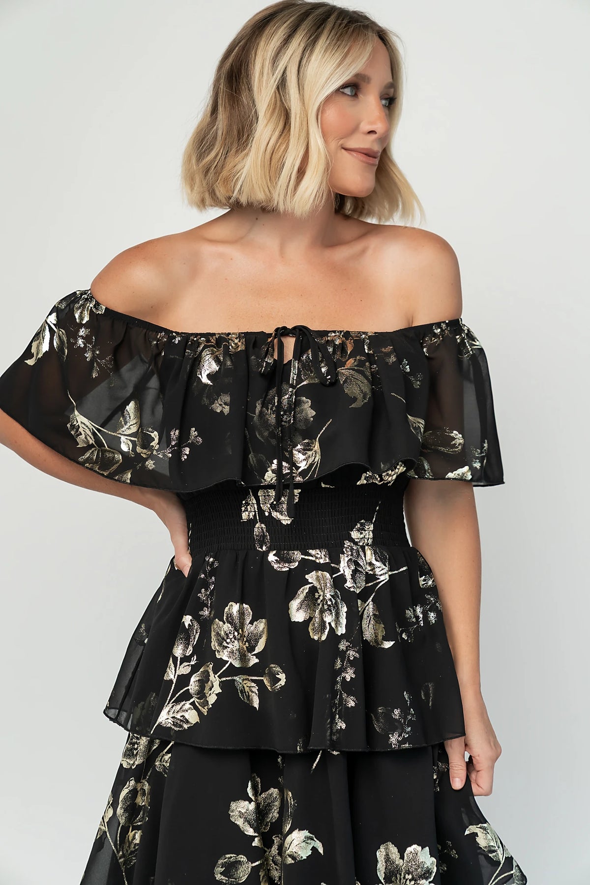 Carina Off Shoulder Maxi Dress in Black + Gold with floral print, ruffle neckline, smocked waist, and tiered chiffon skirt.
