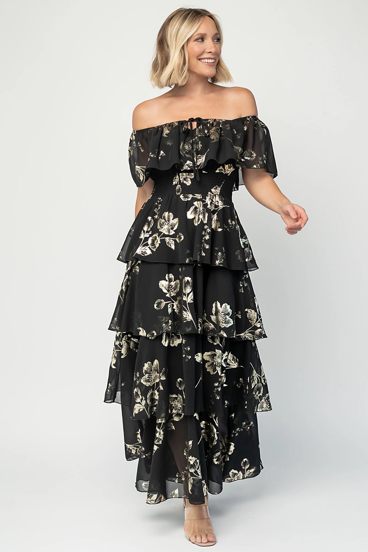 Carina Off Shoulder Maxi Dress in Black + Gold with floral print, ruffle neckline, smocked waist, and tiered chiffon skirt.