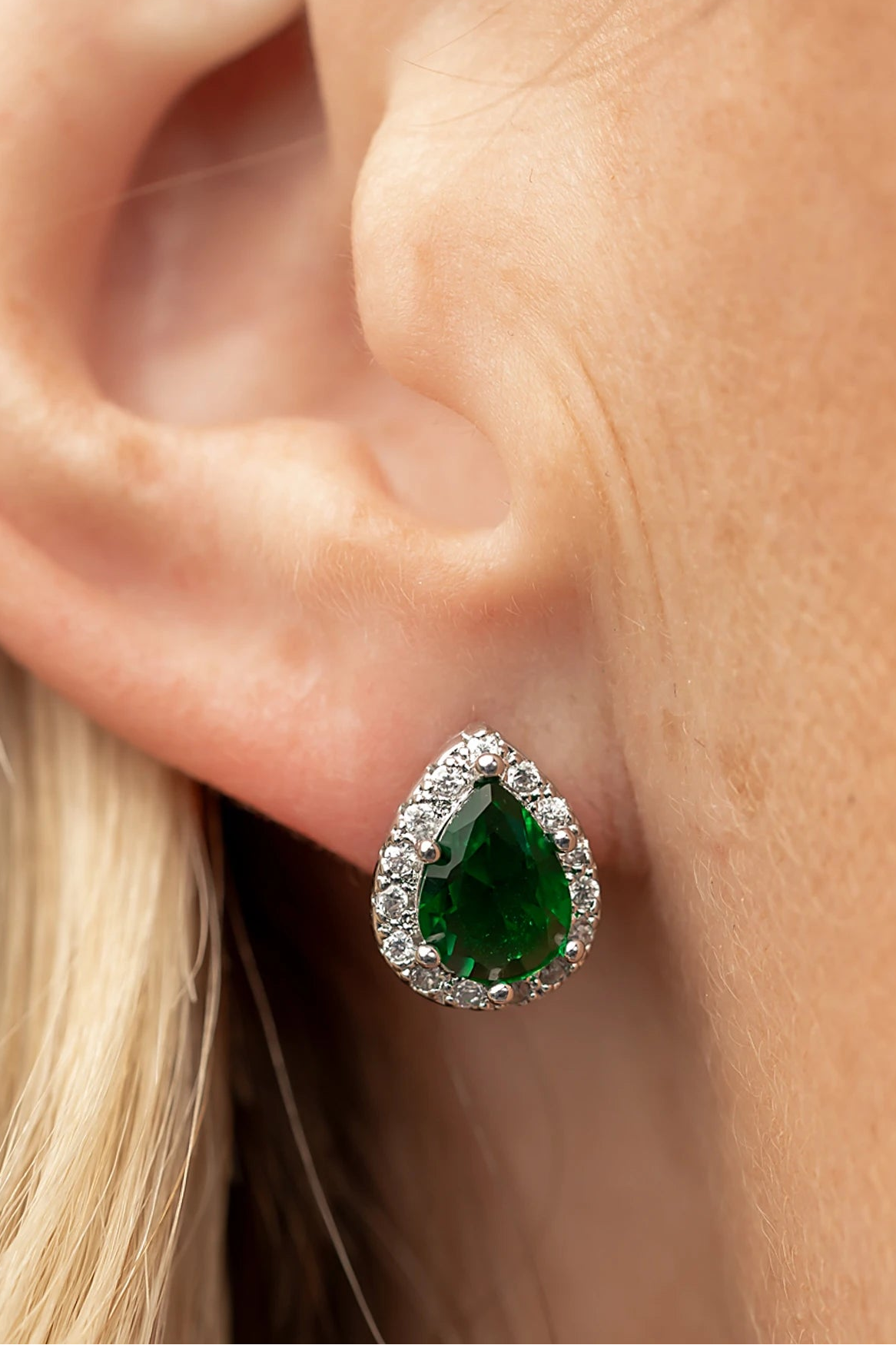 Dacia Pear Cut Stud Earrings in Emerald with pear-cut green stones, clear stone halos, and silver-tone settings.