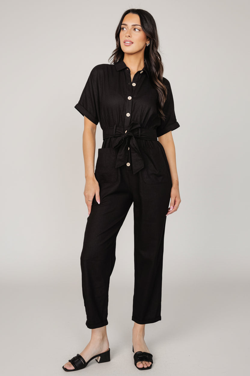 Side view of the Dallas jumpsuit in black, showing the elastic waistband, self-tie sash and slightly cropped, tapered pant silhouette.