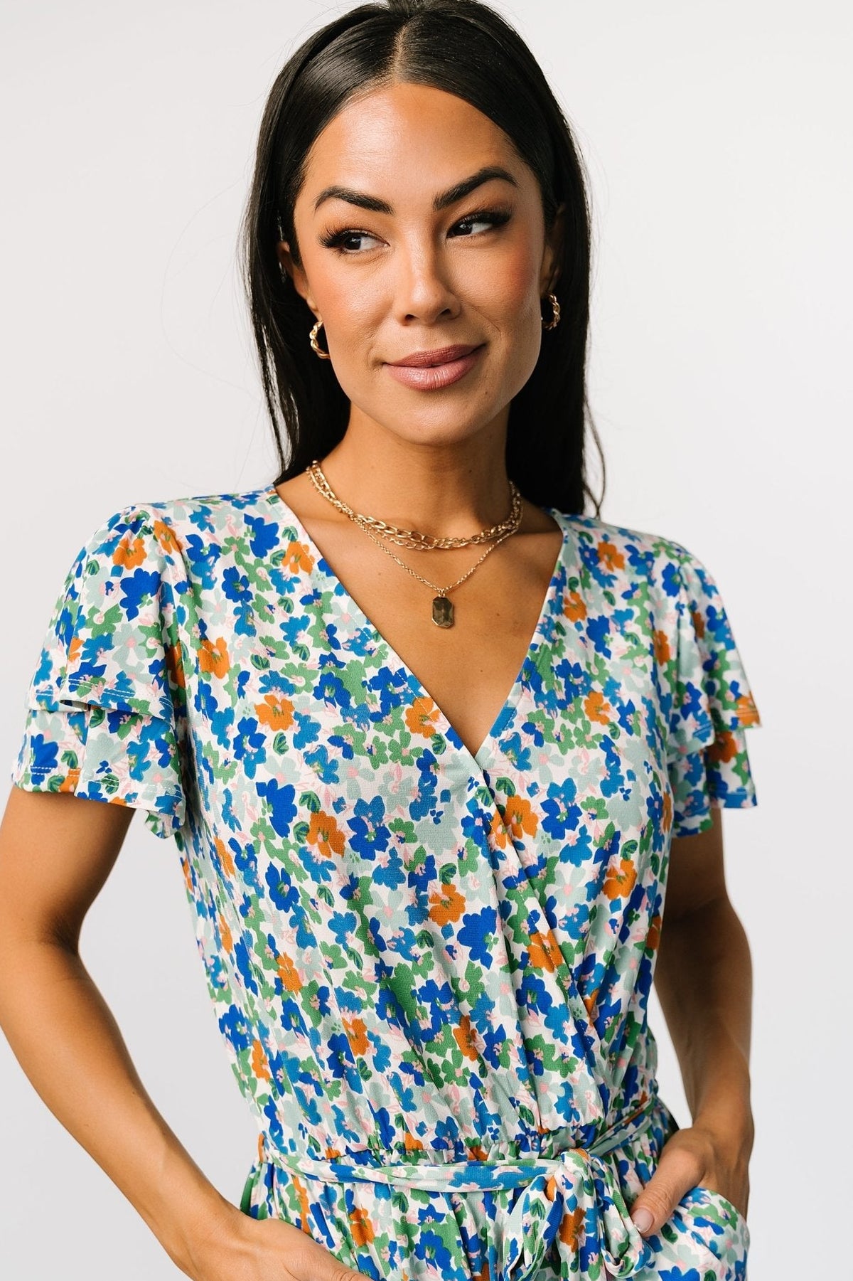 Close-up of sleeve layering and snap-button closure at the surplice neckline on the blue and green multi floral romper.