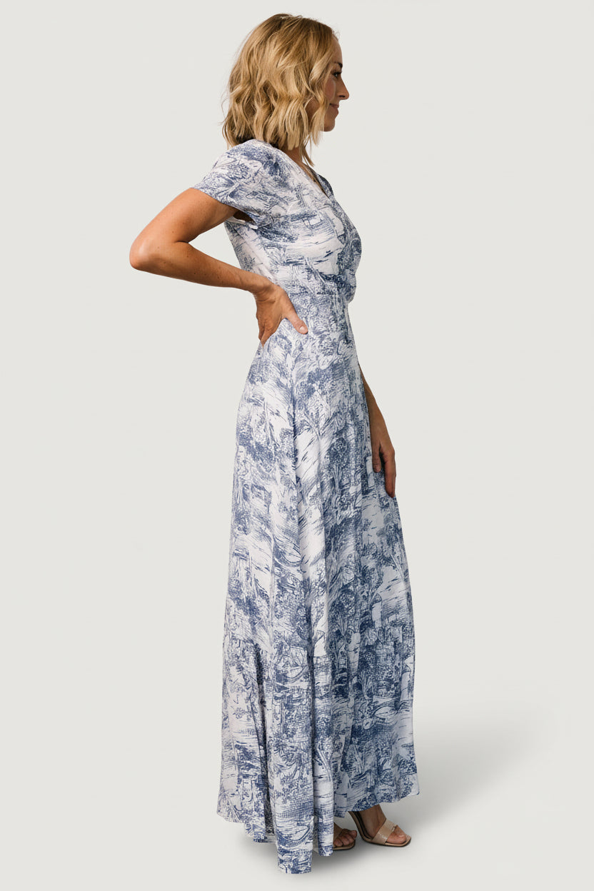 Model wearing the white and blue print wrap maxi in an outdoor garden setting, showing movement and versatile styling.