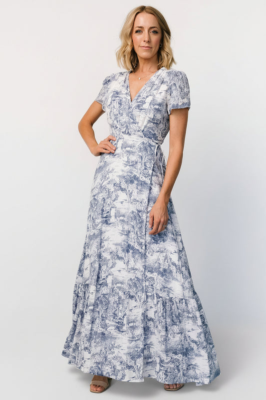 Front view of white maxi wrap dress with dusty blue print, surplice neckline and tied waist on a model.