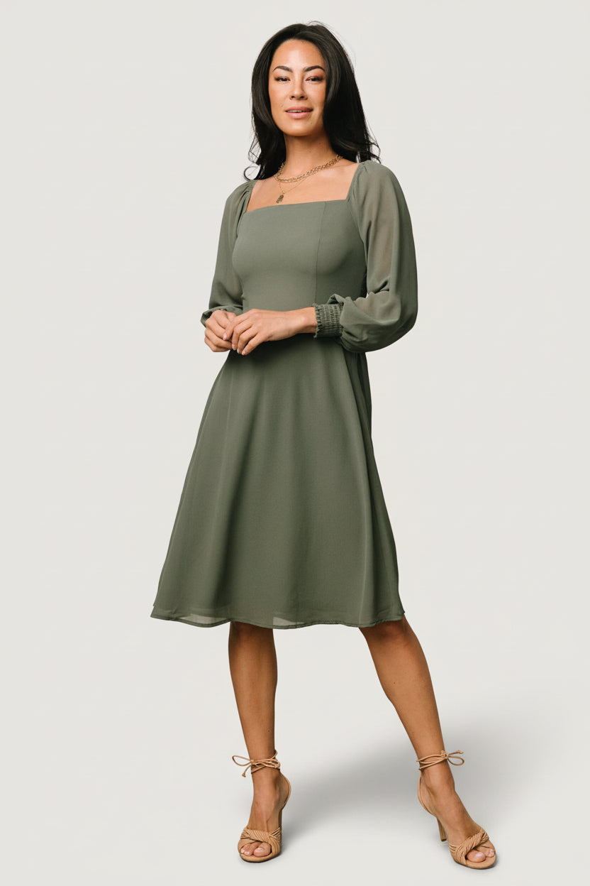 Front view of a short dark sage chiffon dress with smocked back bodice and lined skirt, on a studio mannequin