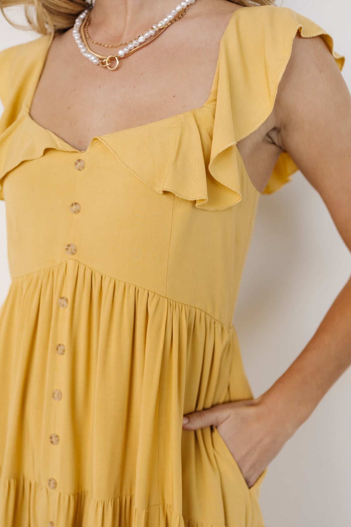 Back view of the dress showing smocked back panel and seam details, with tiered skirt silhouette in golden yellow color.