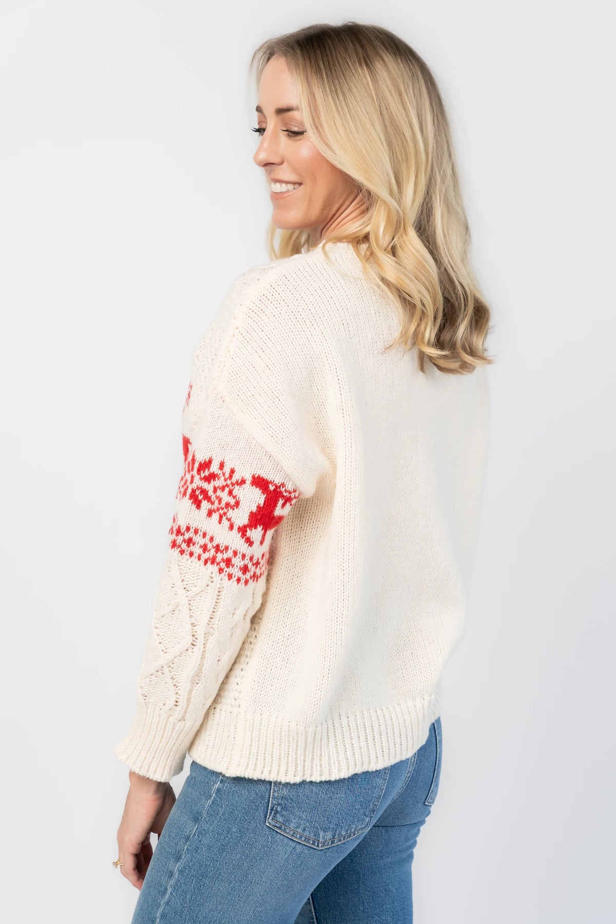 Elyse Sweater in Cream + Red with a Fair Isle reindeer and snowflake pattern, cable knit detailing, and a crew neckline.