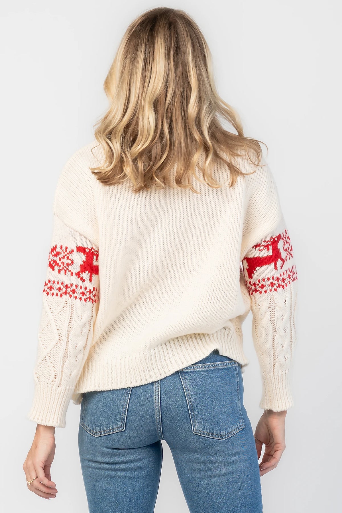 Elyse Sweater in Cream + Red with a Fair Isle reindeer and snowflake pattern, cable knit detailing, and a crew neckline.