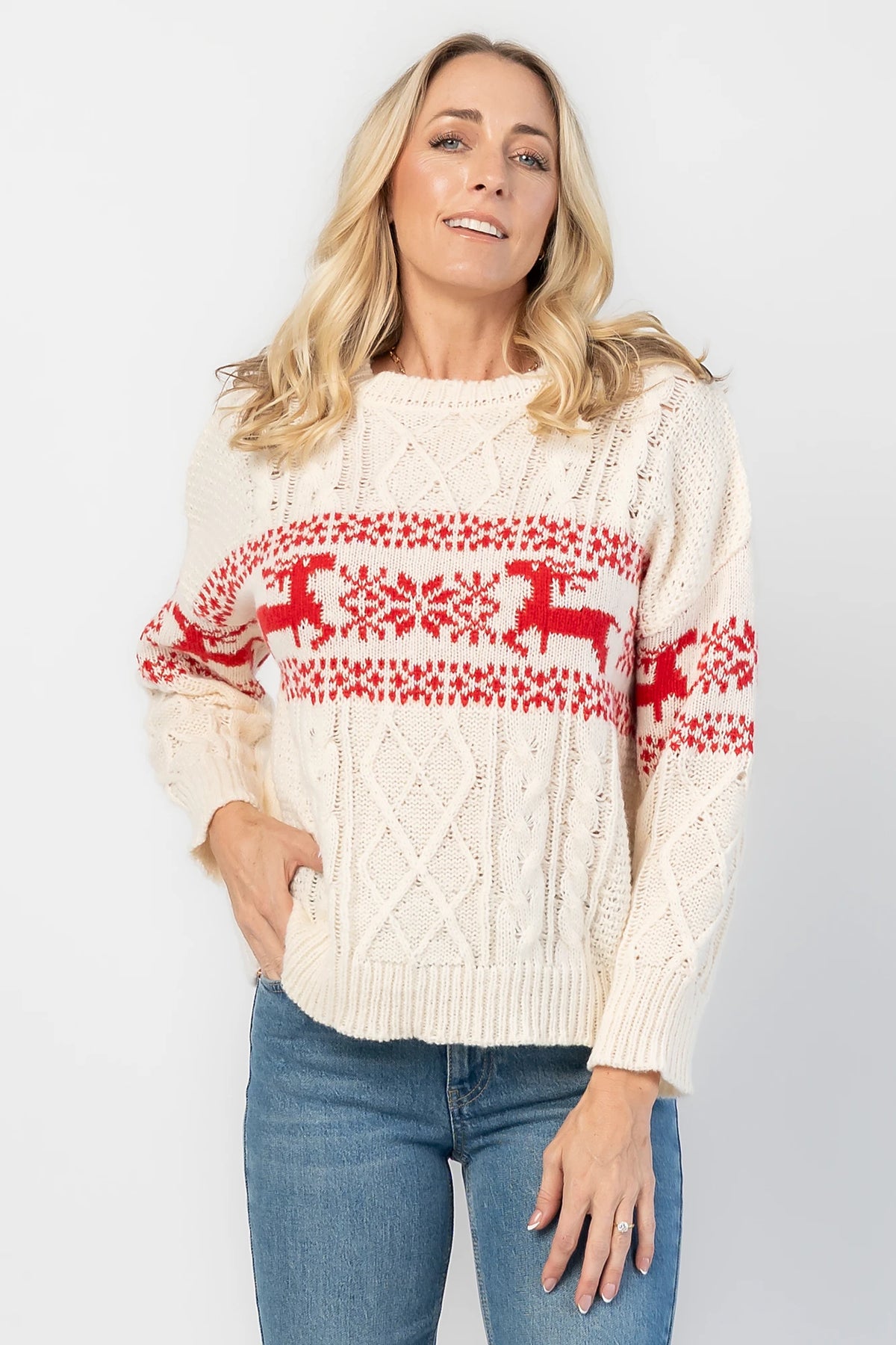 Elyse Sweater in Cream + Red with a Fair Isle reindeer and snowflake pattern, cable knit detailing, and a crew neckline.