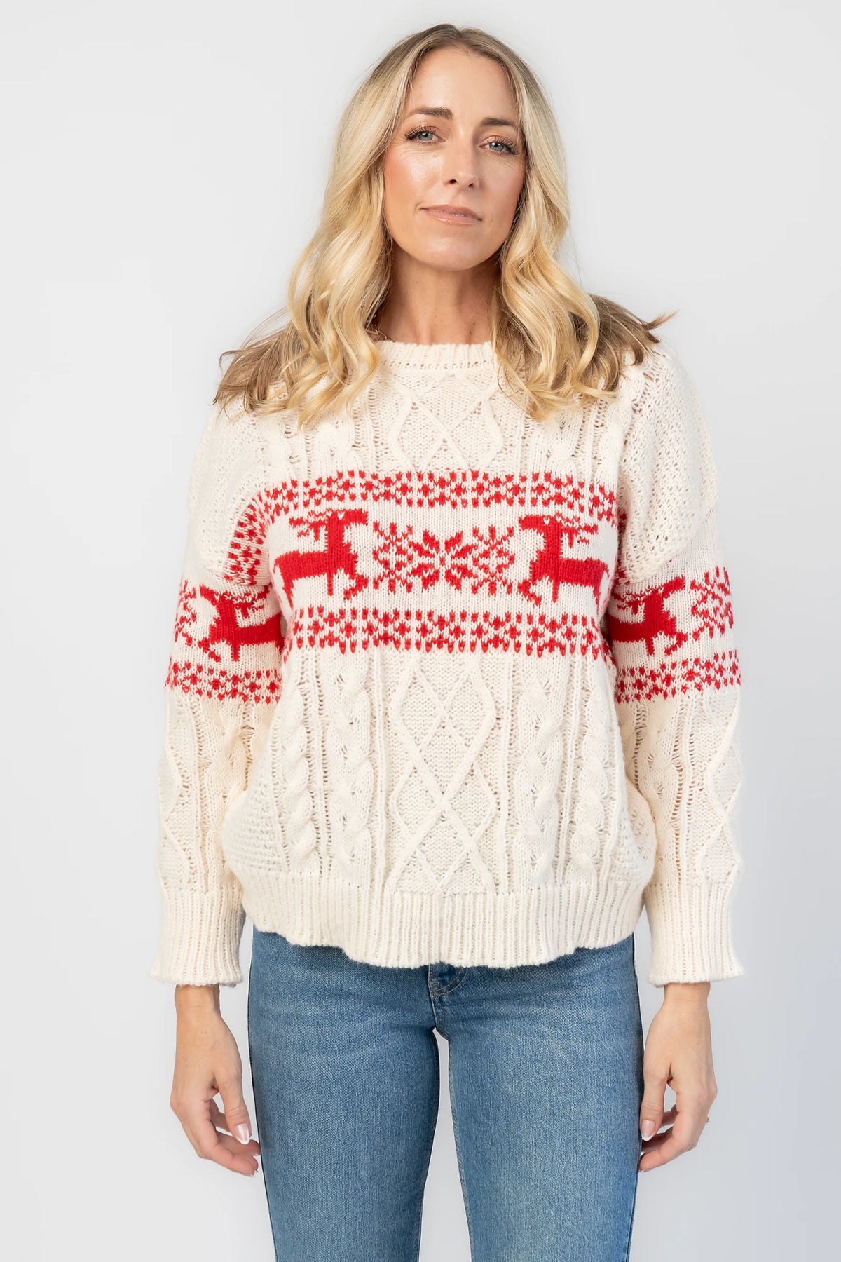 Elyse Sweater in Cream + Red with a Fair Isle reindeer and snowflake pattern, cable knit detailing, and a crew neckline.