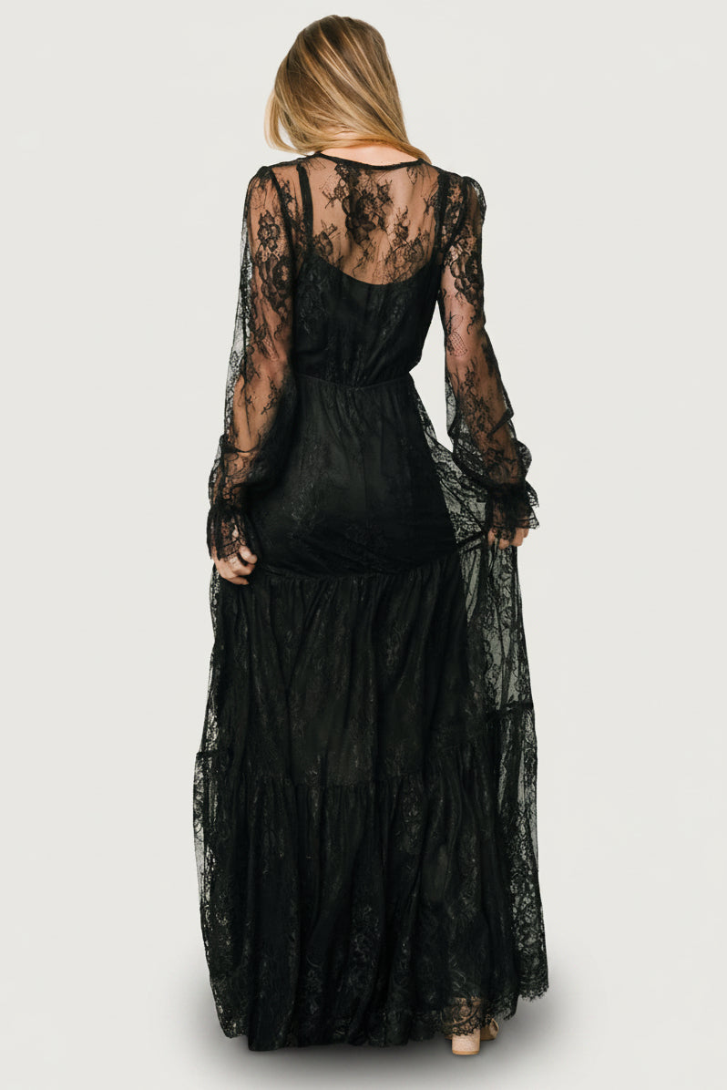Gloria Lace Maxi Dress in Black with deep V-neck, sheer long sleeves, elastic waist, and three-tiered lace skirt.