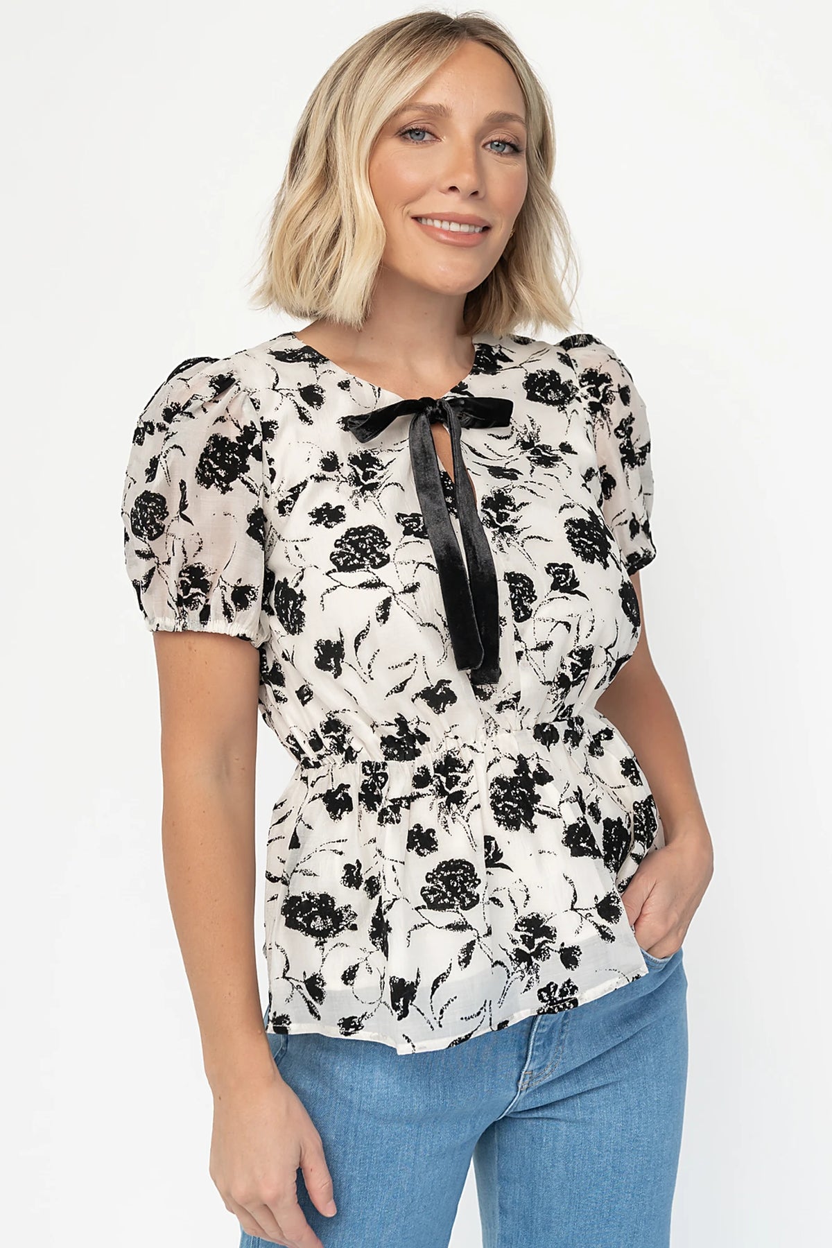 Gwenyth Peplum Blouse in Ivory + Black with velvet florals, front bow, puff sleeves, and elastic peplum waist.