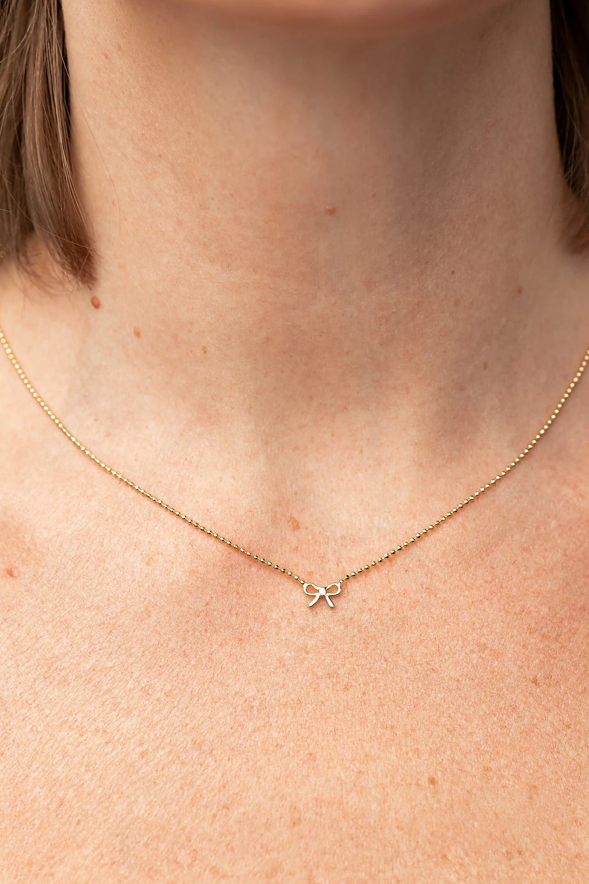 Holly Ribbon Bow Necklace in Gold with a dainty gold-tone chain and petite ribbon bow charm.
