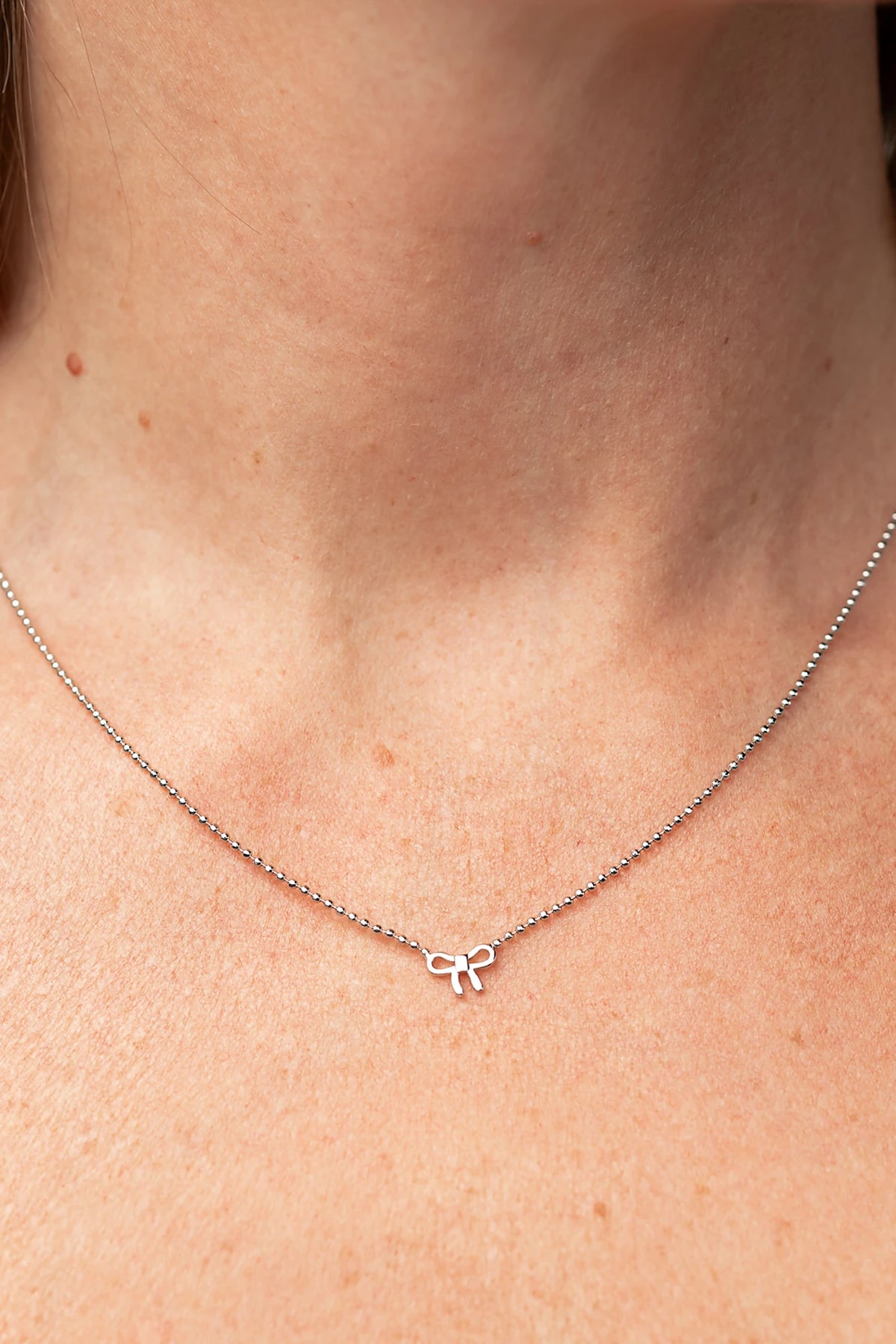 Holly Ribbon Bow Necklace in Silver with a dainty silver-tone chain and petite ribbon bow charm.