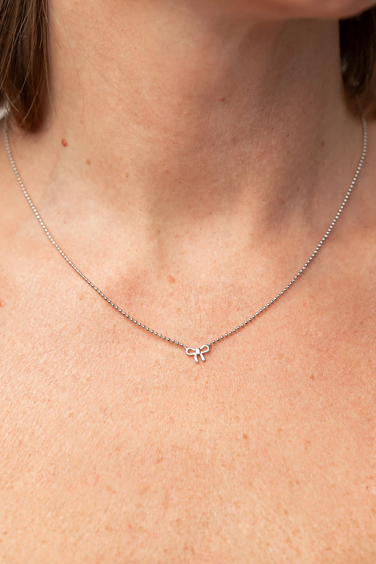 Holly Ribbon Bow Necklace in Silver with a dainty silver-tone chain and petite ribbon bow charm.