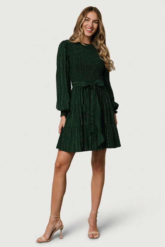Close-up of sleeve detail highlighting long wide sleeve with smocked cuff and delicate ruffle edge in dark green fabric.