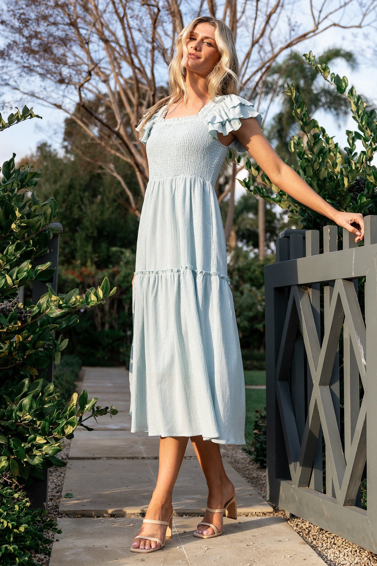 Front view of light blue smocked midi dress with square neckline, ruffle cap sleeves, smocked bodice, and hidden side pockets for casual wear.