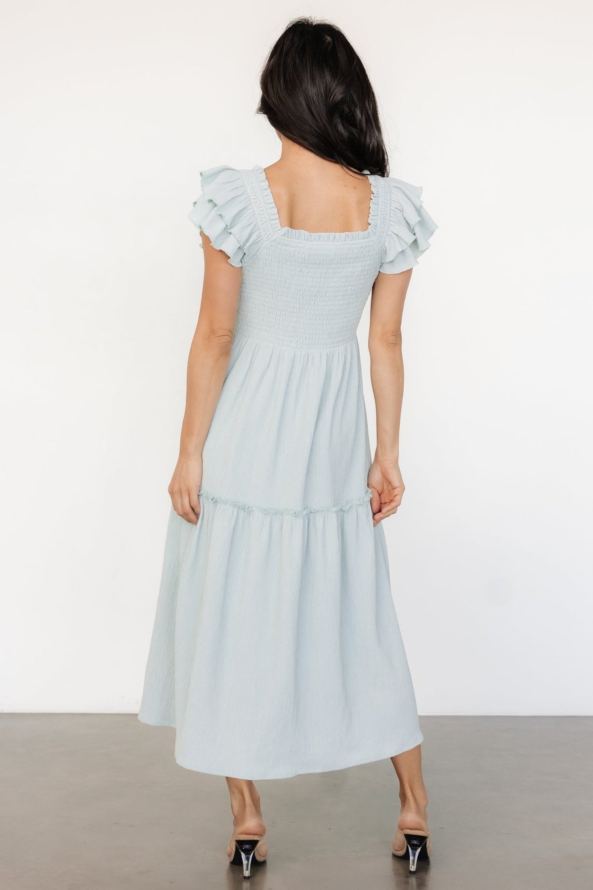 Close-up of smocked bodice and square neckline on light blue midi dress showing textured stretch fabric and delicate ruffle cap sleeve detail.