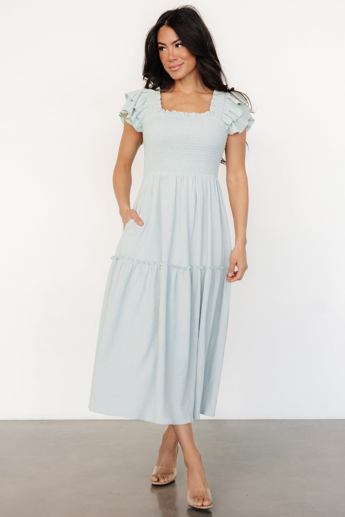 Three-quarter view showing the light blue smocked midi dress silhouette, single-tier skirt, and knee-length lining for modest coverage and movement.