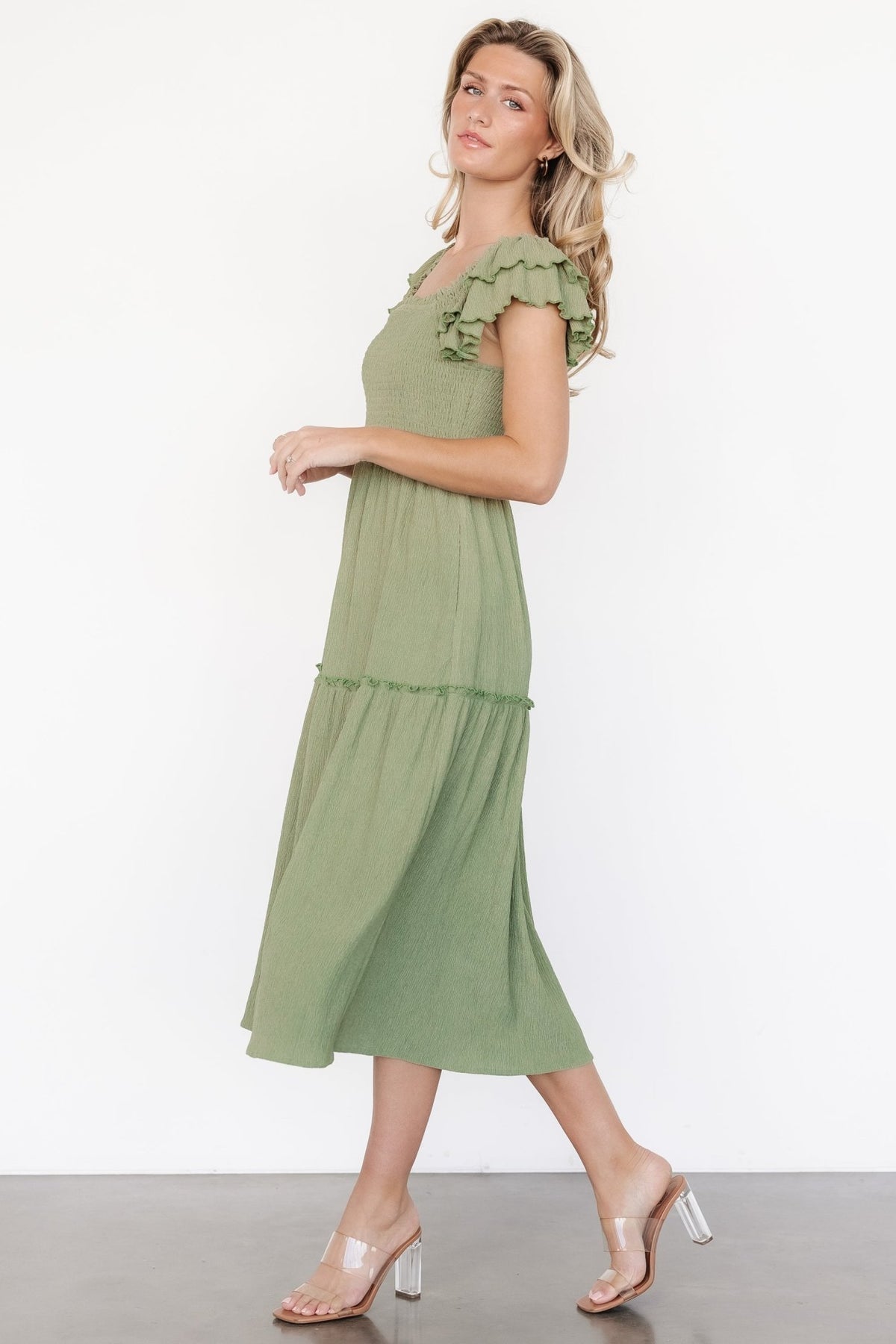 Side profile of Jacie Smocked Midi Dress in sage on model, revealing knee-length lining, flow of the one-tier skirt, and unlined sleeve silhouette.