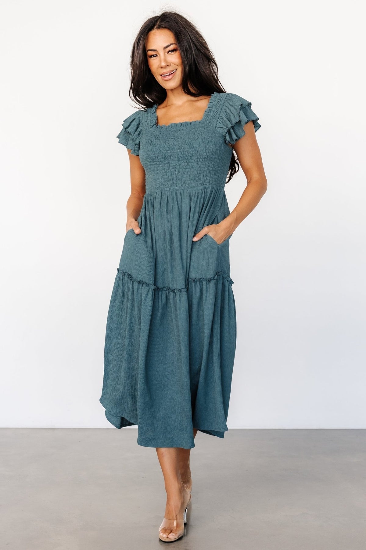 Three-quarter view of the Jacie Smocked Midi Dress in vintage teal, highlighting cap ruffle sleeves, single-tier skirt, and hidden side pockets on model.