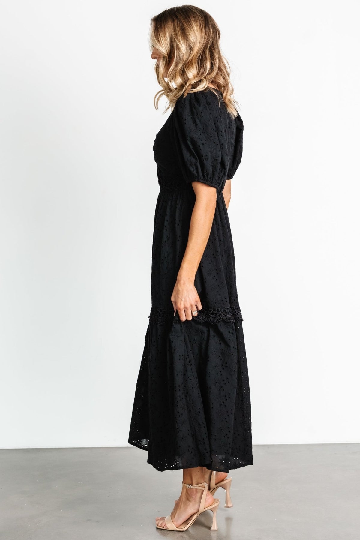 Lifestyle image of the Jackie Eyelet Maxi Dress in black, displaying its tiered silhouette and lace detailing in real-world styling.