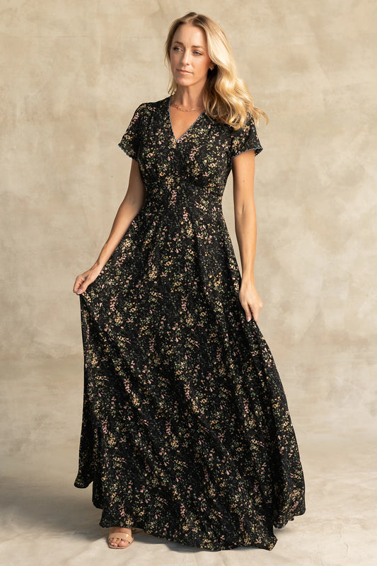 Jada Maxi Dress in Black Floral with V-neckline, blue scalloped trim, flutter sleeves, empire waist, and tie waist.
