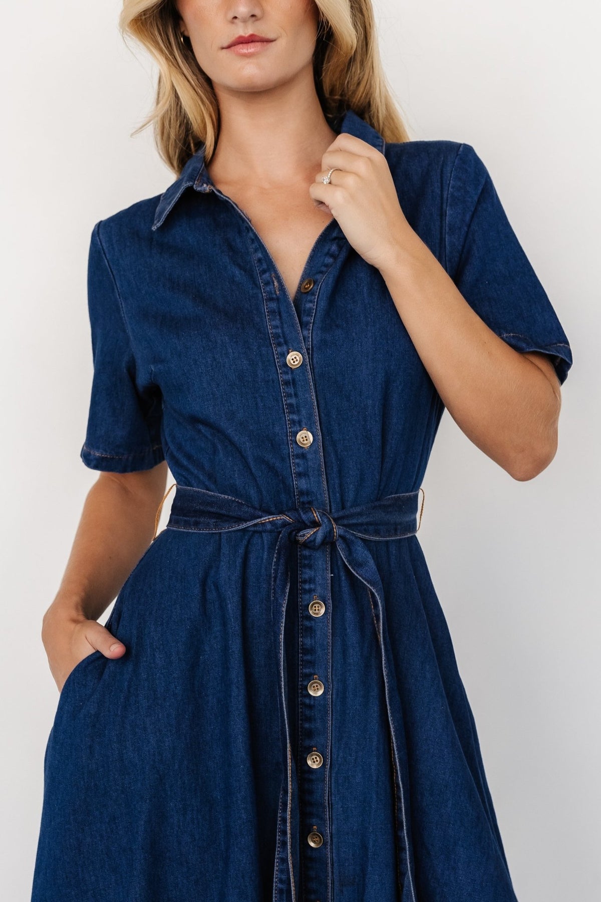 Three-quarter angle showing dark-blue denim fabric, contrast dark-yellow topstitching, and button-front detail.