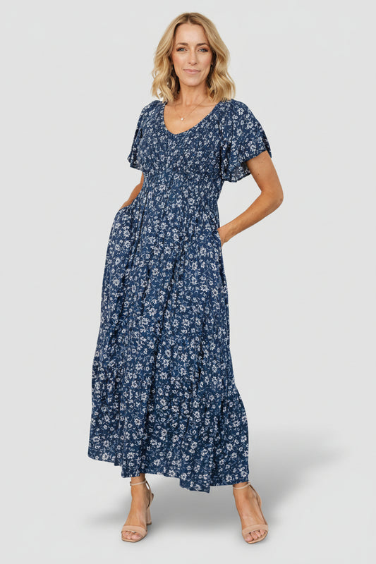 Front view of Joanie Smocked Midi Dress in sapphire blue floral, showing smocked bodice, flutter sleeves, and midi hem.