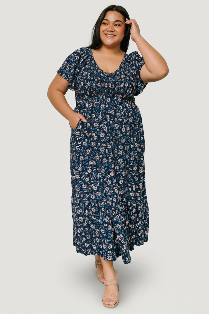 Three-quarter view of Joanie Smocked Midi Dress in blue floral with visible hidden side pocket and flowing skirt movement.