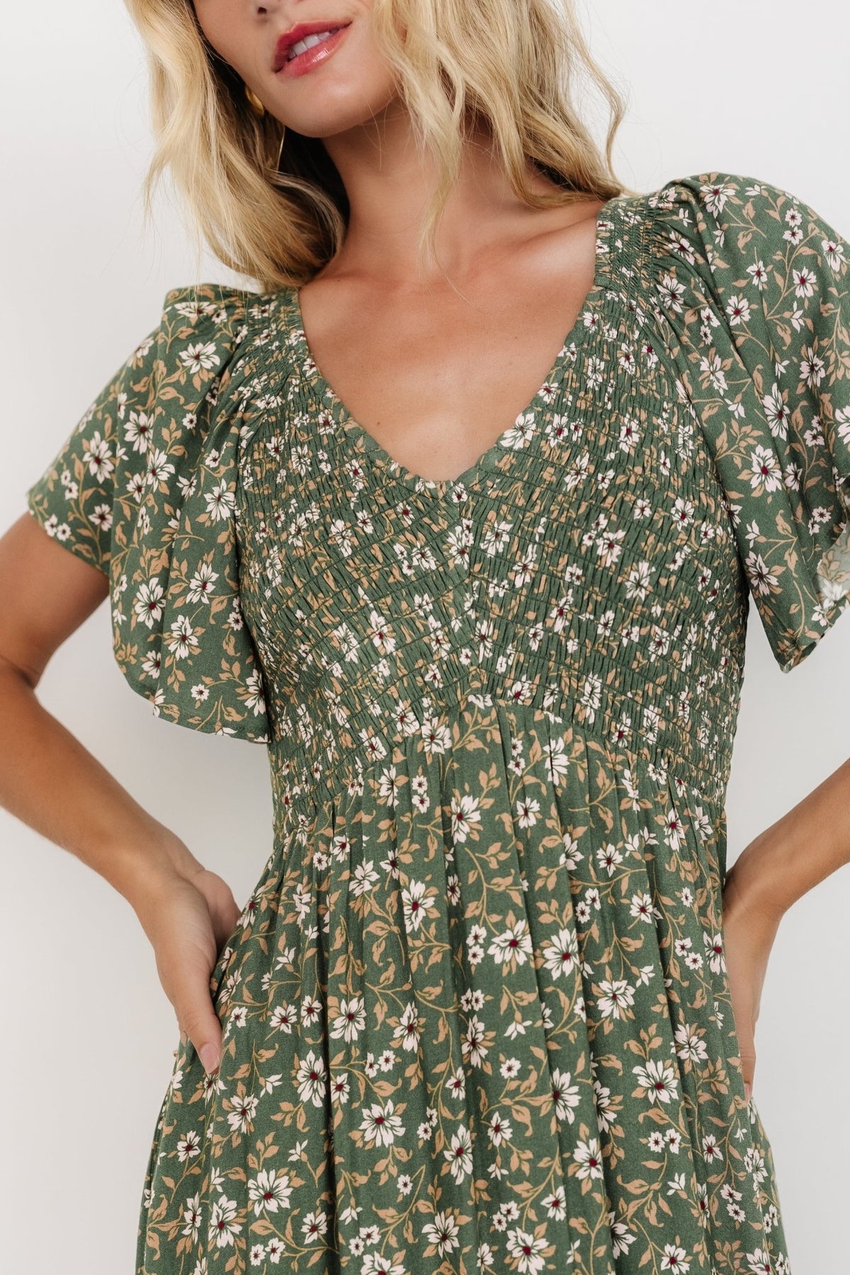 Side view of the dress on model emphasizing the empire waist, flutter sleeve with smocking at the shoulder, and graceful skirt drape.