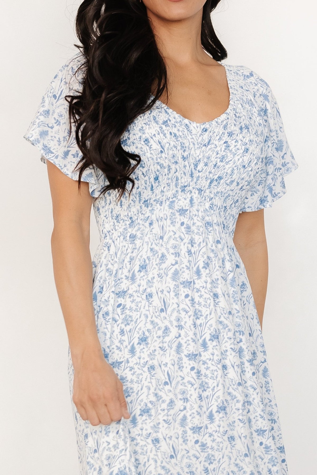 Full-length view of the white and blue floral Joanie dress on a model, highlighting relaxed empire waist and single-tier flowy skirt with pockets.