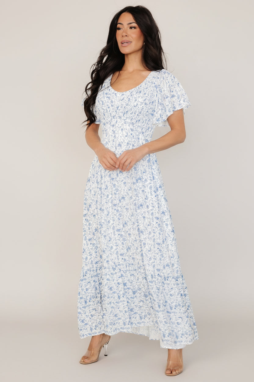 Front view of Joanie smocked midi dress in white with blue floral print, showing smocked bust, wide V-neckline, flutter sleeves, and midi hem.